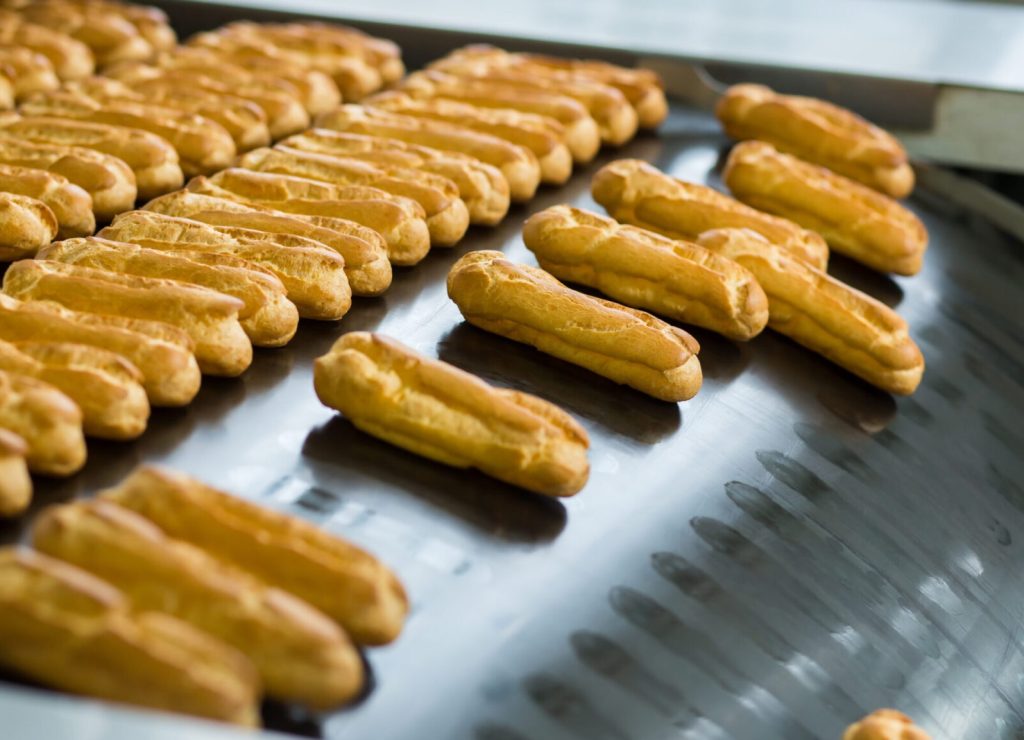 Yellow eclair shells on conveyor. Eclairs slide down conveyor line. High standard of quality. Making the best confectionery.